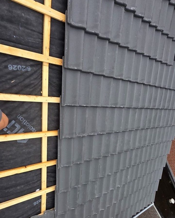 Dakpannen worden teruggelegd op de nieuwe panlatten boven de isolatiefolie
