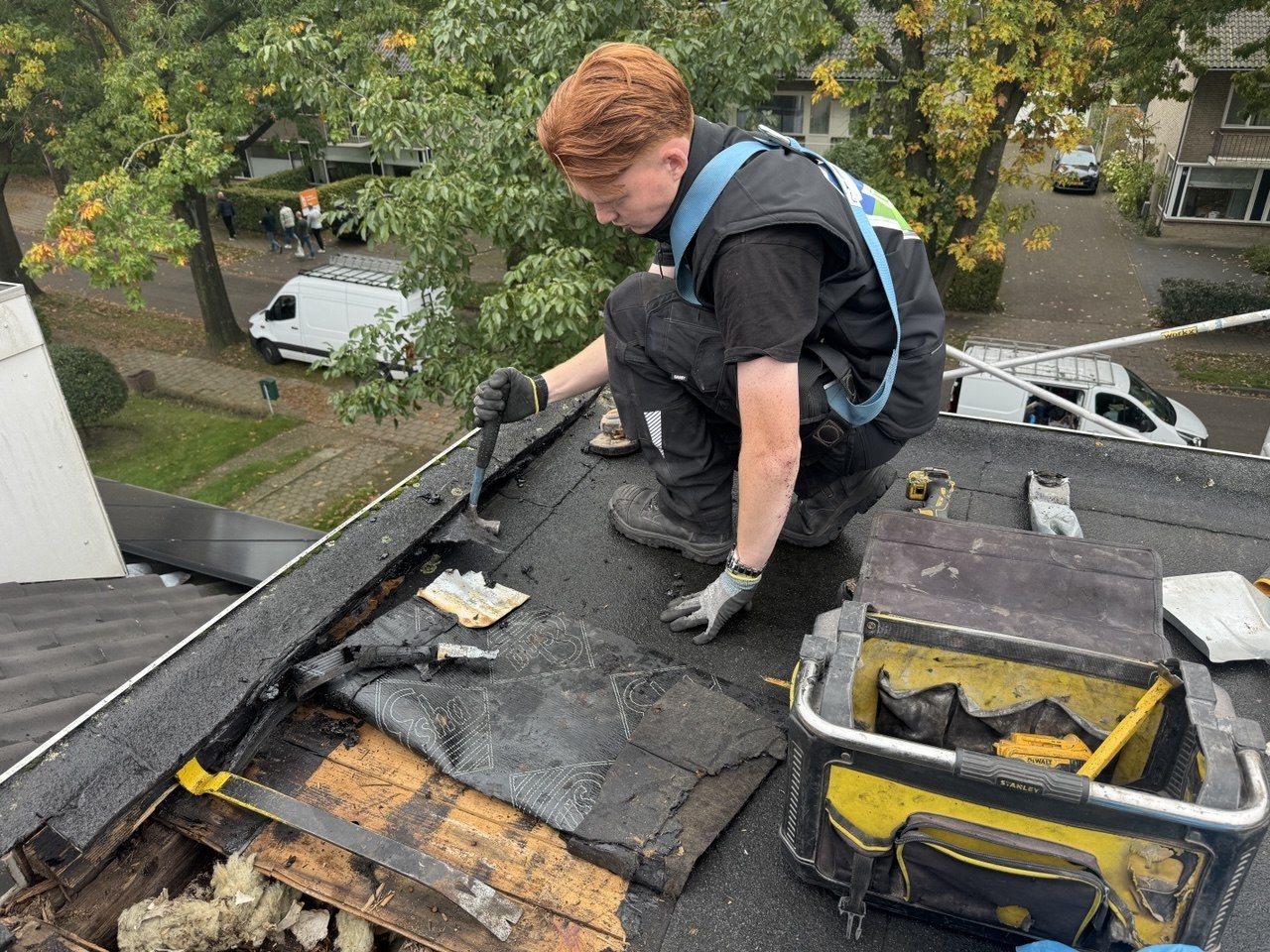 Dakdekker van TBGS in harnas herstelt de dakrand van een plat dak, met de oude dakbedekking verwijderd