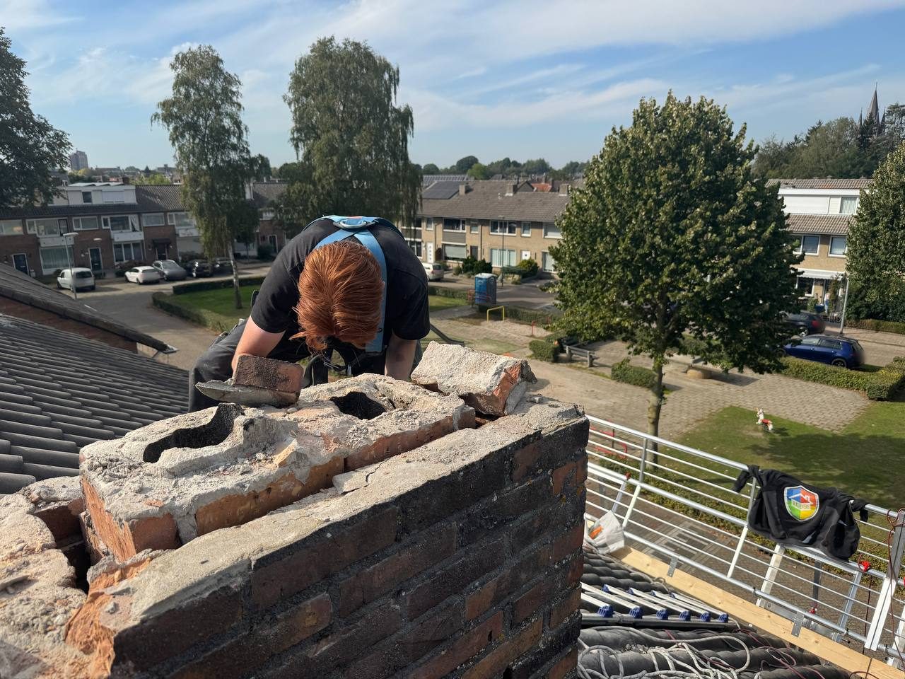 Schoorsteen op een pannendak met collectieve randbeveiliging langs de dakrand en een dakladder met nokhaken